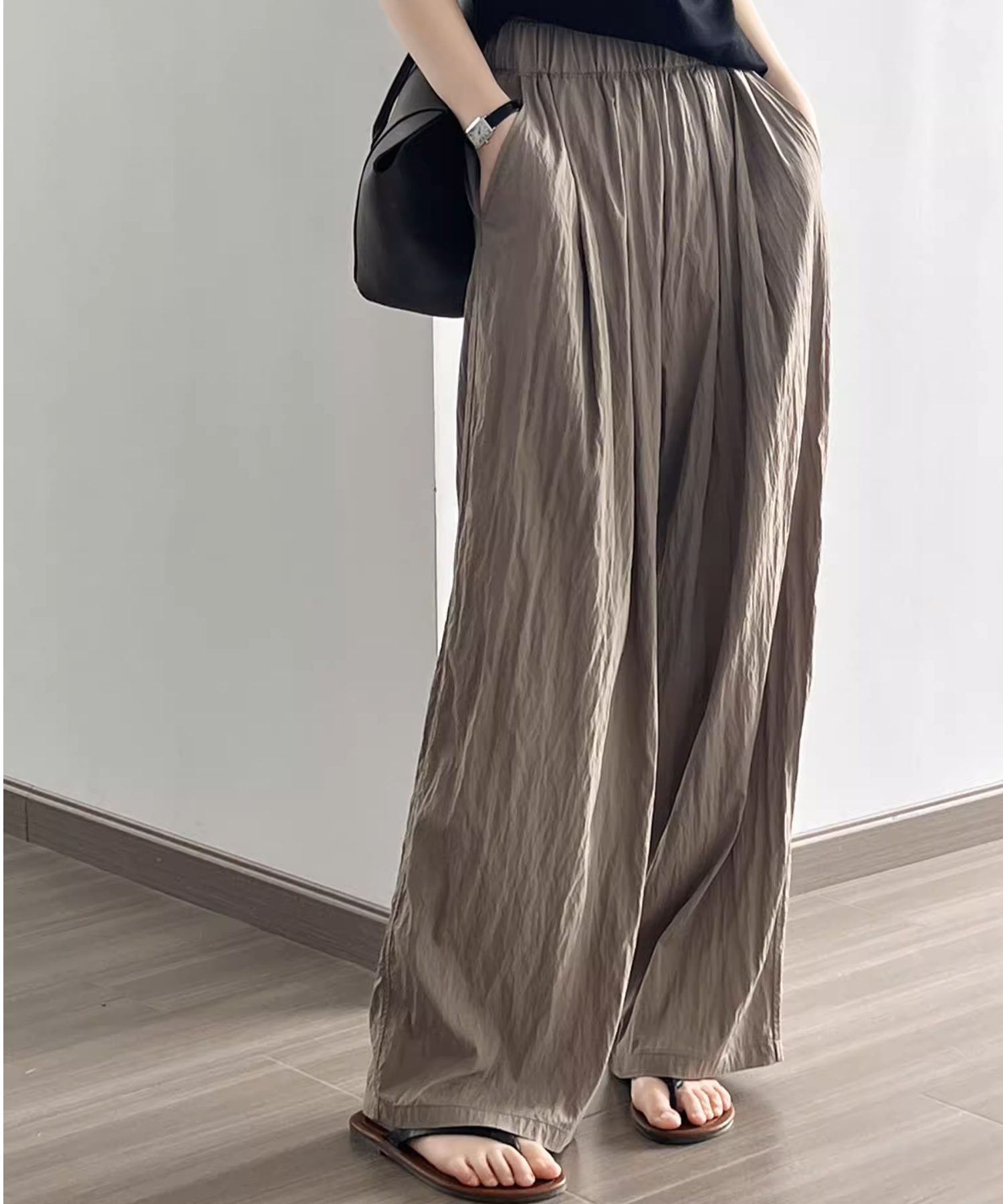 コーヒー色のウエストゴムでシワ加工の施されたワイドパンツを着用した女性。サンダルと合わせている。