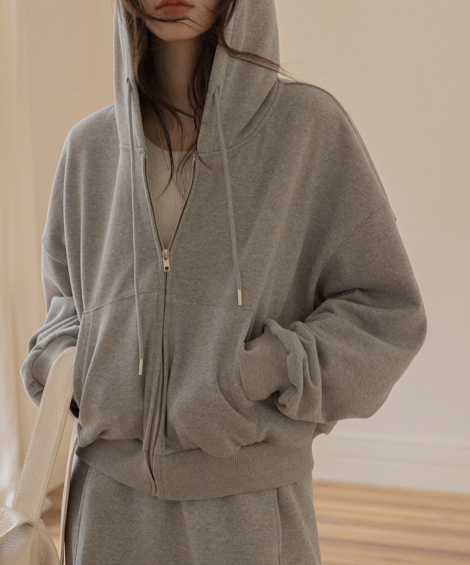 グレーのスウェットジップアップパーカーのフードをかぶった女性の半身画像。