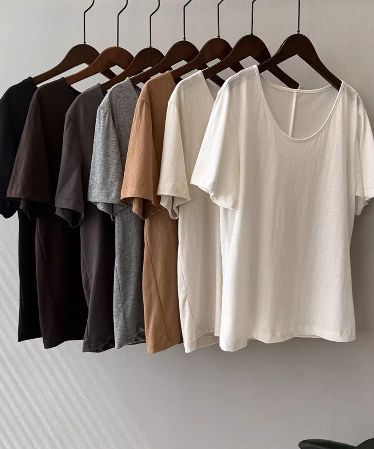 ブラック、ブラウン、ダークグレー、ライトグレー、キャメル、アプリコット、ホワイトのTシャツがハンガーにかけらてて並べられている静物画像。