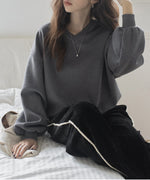 グレーのVネックバルーンスリーブトップスと黒のベロアワイドパンツを合わせた女性が座っている写真。