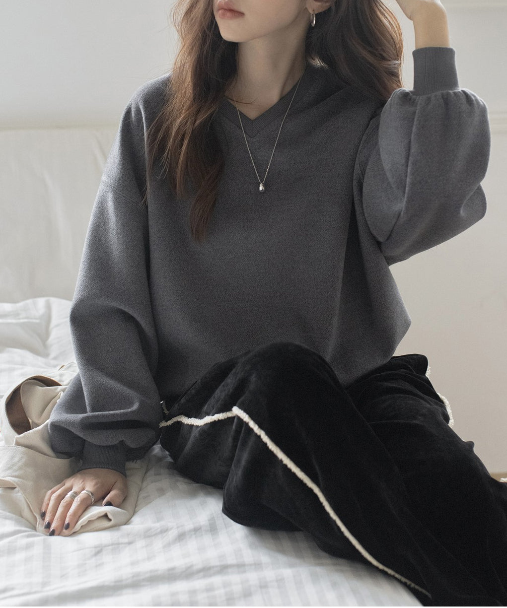 グレーのVネックバルーンスリーブトップスと黒のベロアワイドパンツを合わせた女性が座っている写真。