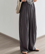 ダークグレーのパンツを着用した女性がベージュ色のバッグを肩にかけた画像。
