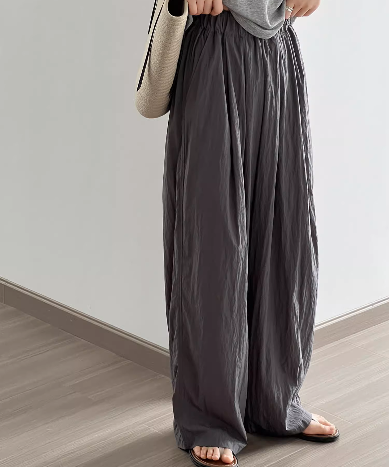 ダークグレーのパンツを着用した女性がベージュ色のバッグを肩にかけた画像。