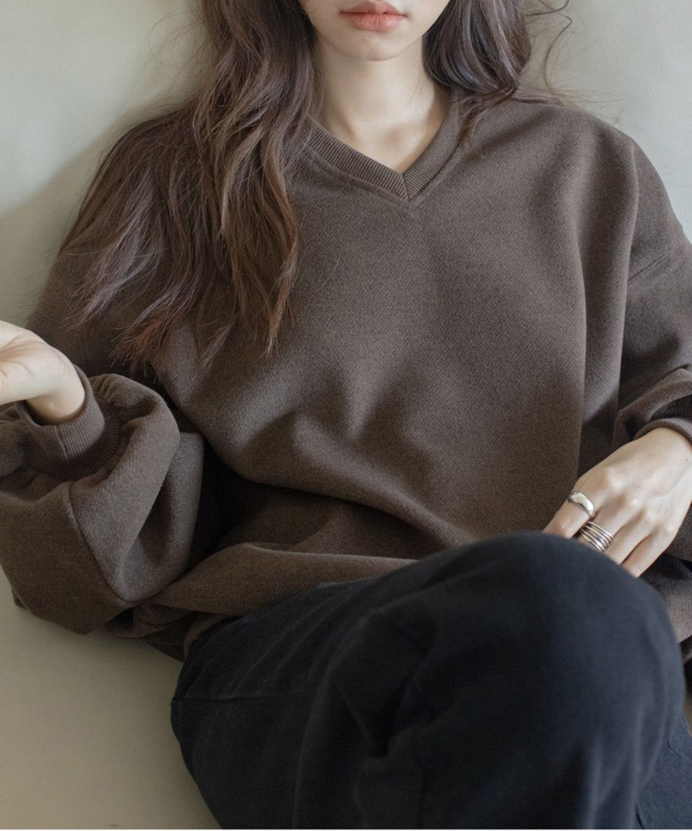 ブラウンのVネックバルーンスリーブトップスを着た女性のクローズアップ。下は黒のパンツを着用している。