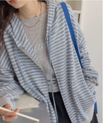 ライトブルーとグレーの細いボーダー柄のジップアップパーカーを着用した女性の半身。インナーにはグレーのトップス、ボトムスには黒のミニスカートやデニムを合わせたカジュアルスタイル。肩にブルーのバッグをさげている。