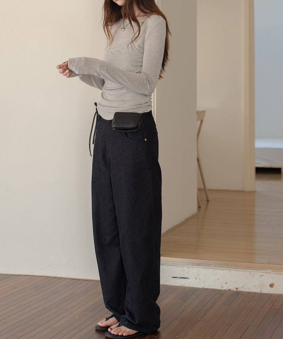 グレーのトップスとブラックのワイドレッグパンツを着たモデルが部屋で立っている画像。シンプルでスタイリッシュなコーディネートが可能。