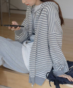グレーと白の細いボーダー柄のジップアップパーカーを着用した女性の半身。スマホを手にもって座っている写真。