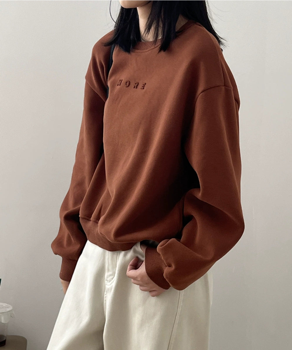 オレンジのエンボス加工スウェットシャツとベージュのパンツを着用した女性のショット。