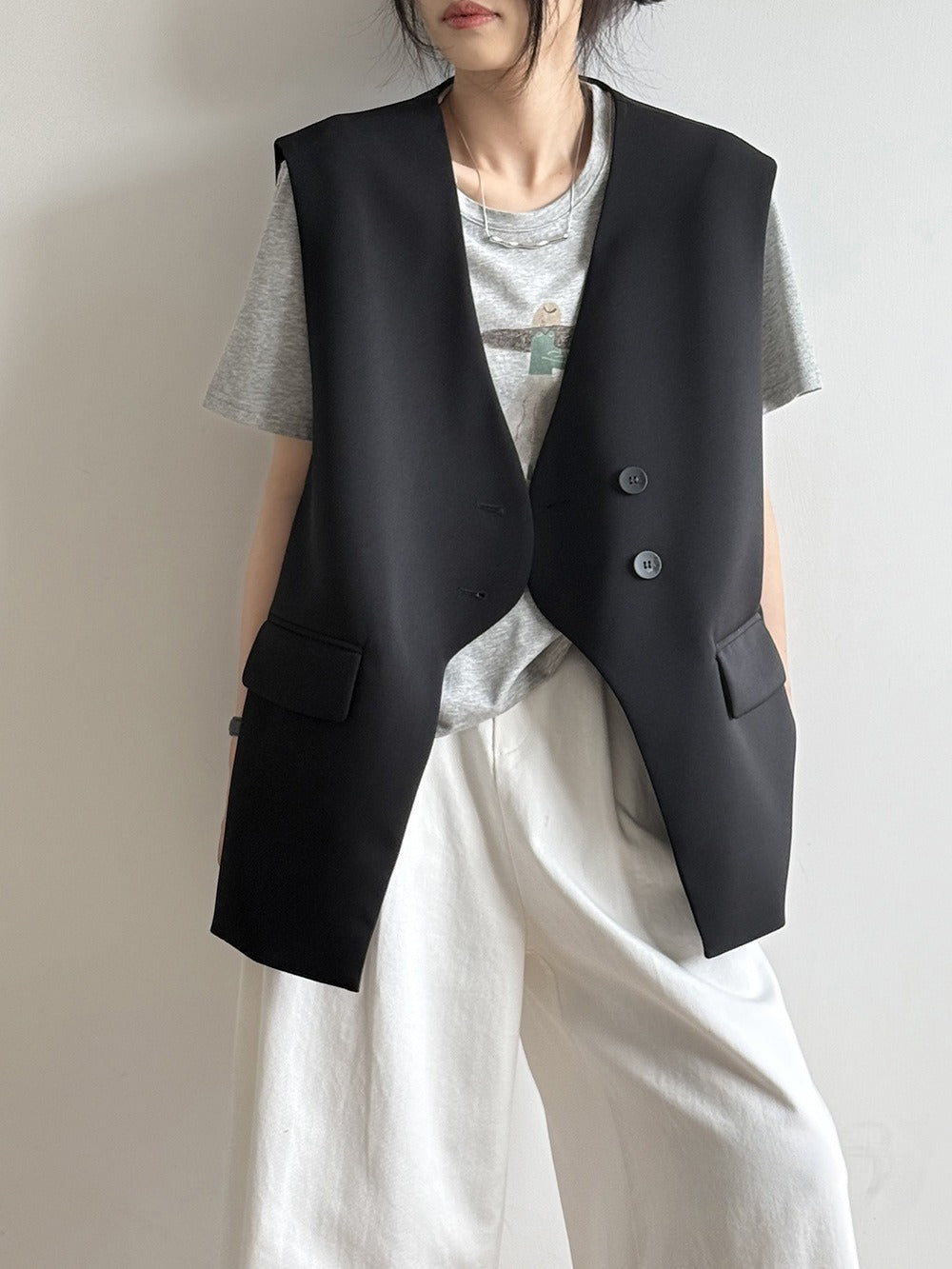 黒のオーバーサイズテーラードジレに、薄いグレーのTシャツと白のボトムスを合わせた女性の側面からのクローズアップ。