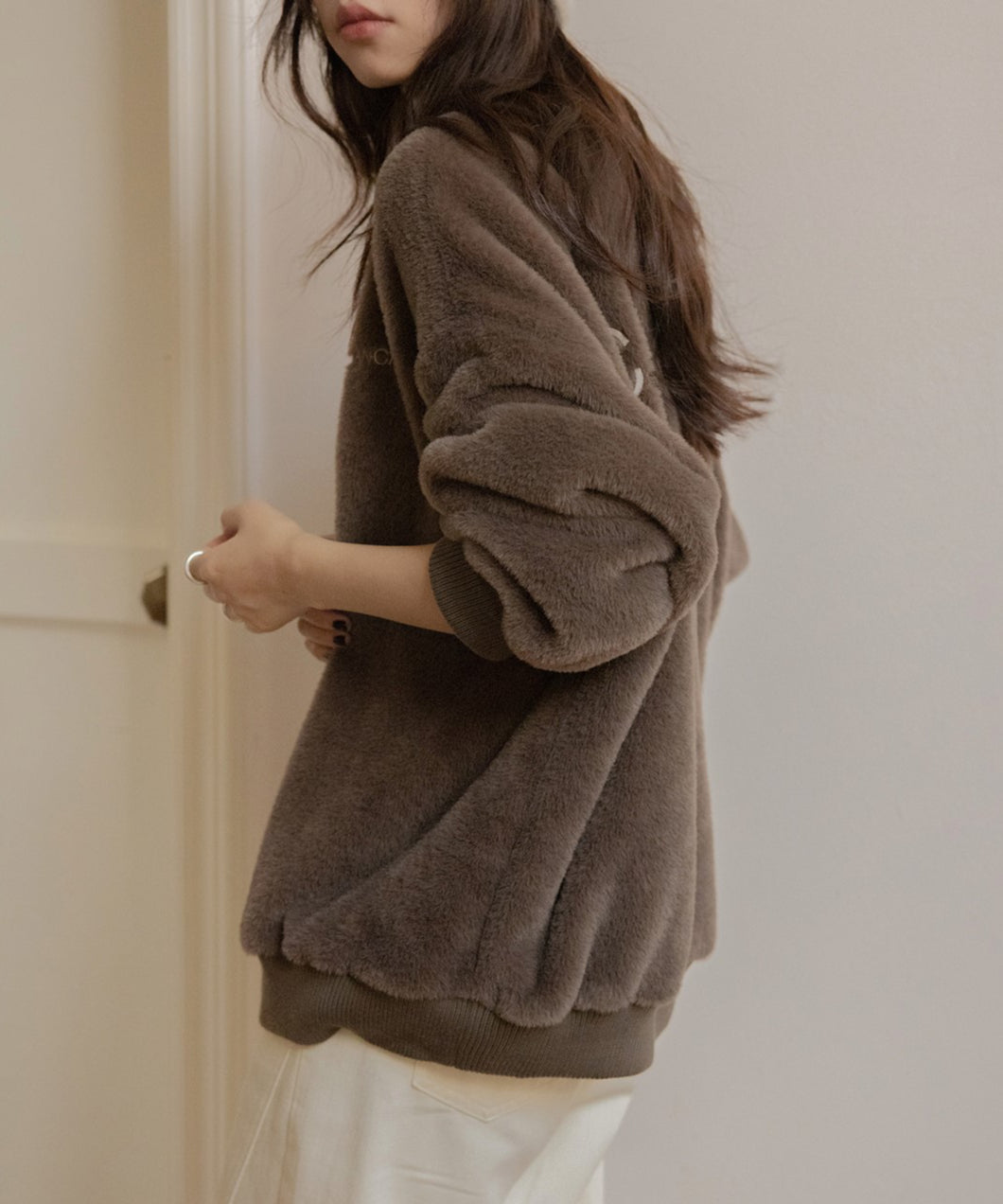 ブラウンのふわふわしたボア素材のプルオーバーを着た女性の横からのクローズアップ。白いパンツとコーディネートした画像。