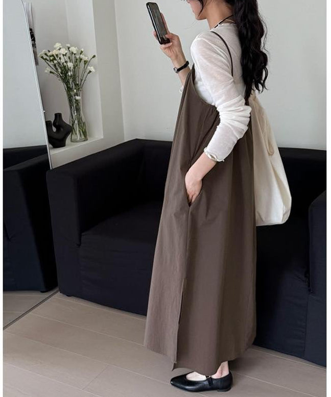 白い長袖トップスに茶色いロングキャミソールワンピースを着用し、スマートフォンを持っている女性のサイドスタイル。