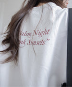 白のオーバーサイズスウェットの背面クローズアップ。背中の上部には「Balmy Night Pink Sunsets」の赤茶色のプリントが施されている。