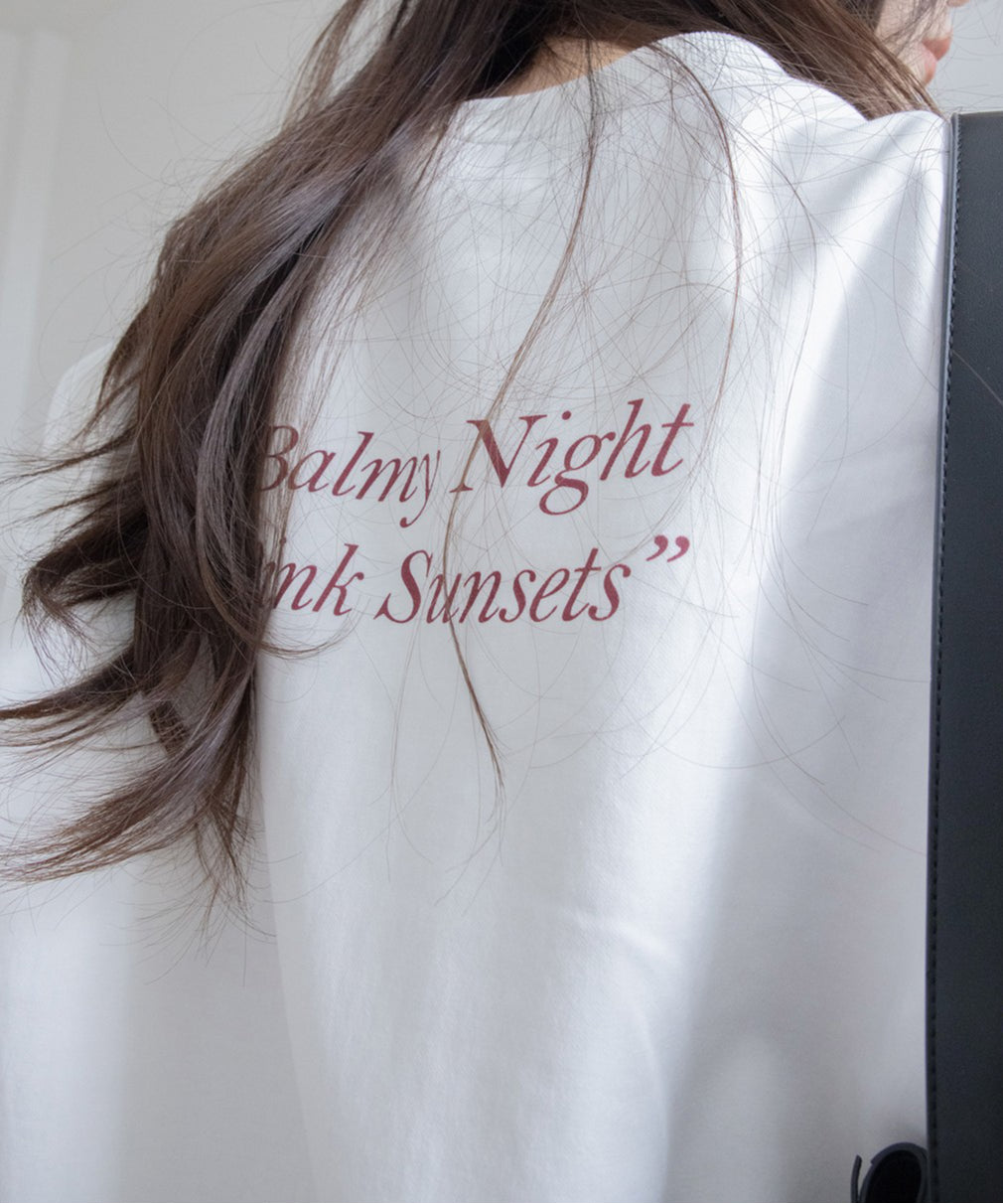 白のオーバーサイズスウェットの背面クローズアップ。背中の上部には「Balmy Night Pink Sunsets」の赤茶色のプリントが施されている。
