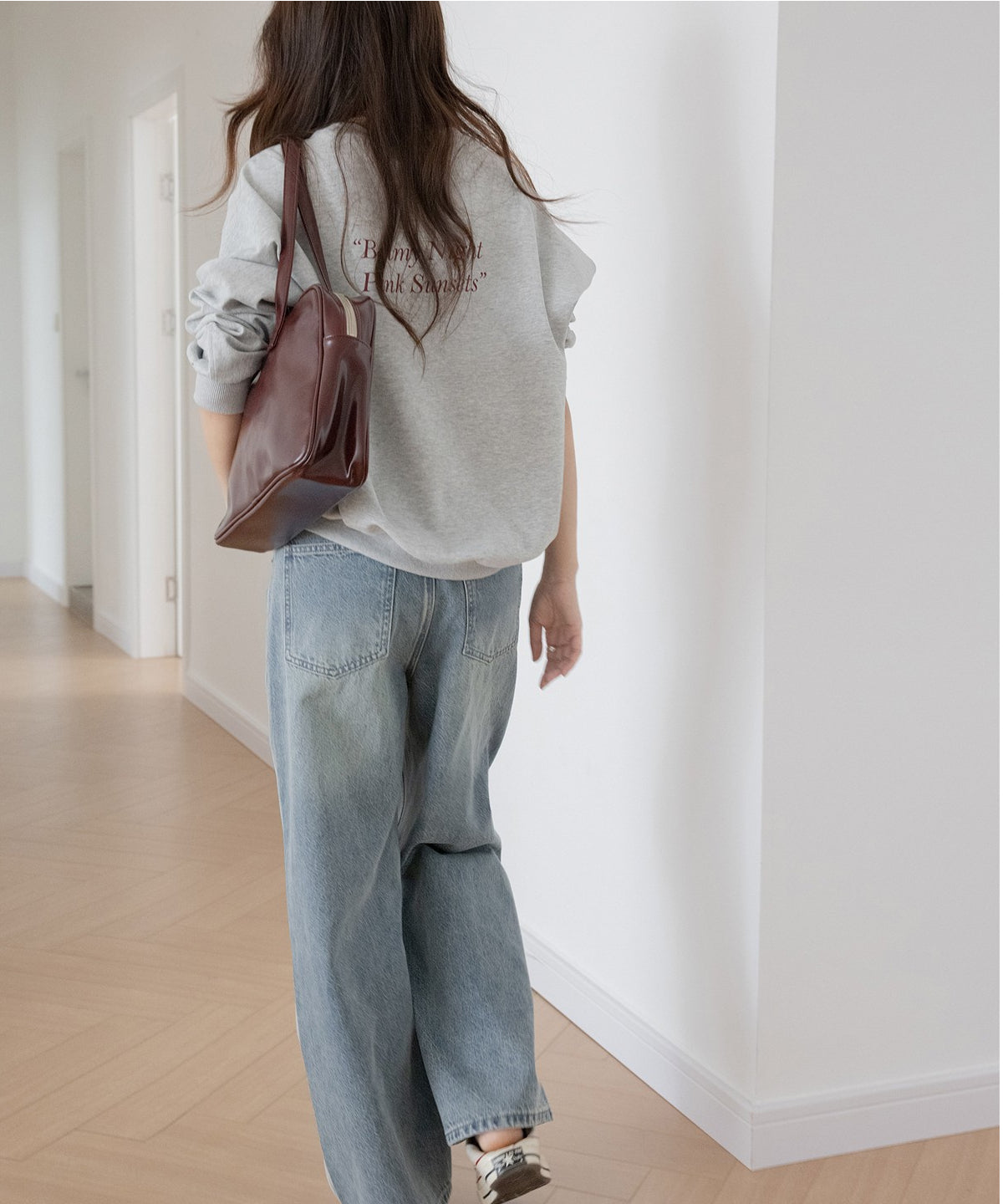 グレーのオーバーサイズスウェットを着用した女性の後姿。茶色のバッグを肩にかけている。