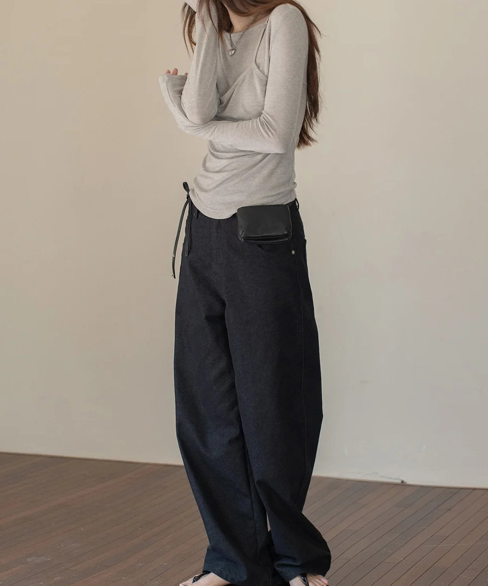 ライトグレーのレイヤードデザインのロングスリーブトップスを着用し、黒のミニバッグをウエストに持った女性。長い袖丈とサムホールが特徴。