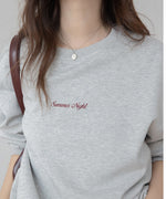 グレーのオーバーサイズスウェットを着用した女性のクローズアップ。胸元には「Summer Night」の赤茶色の刺繍ロゴがあり、茶色のバッグを肩にかけている。