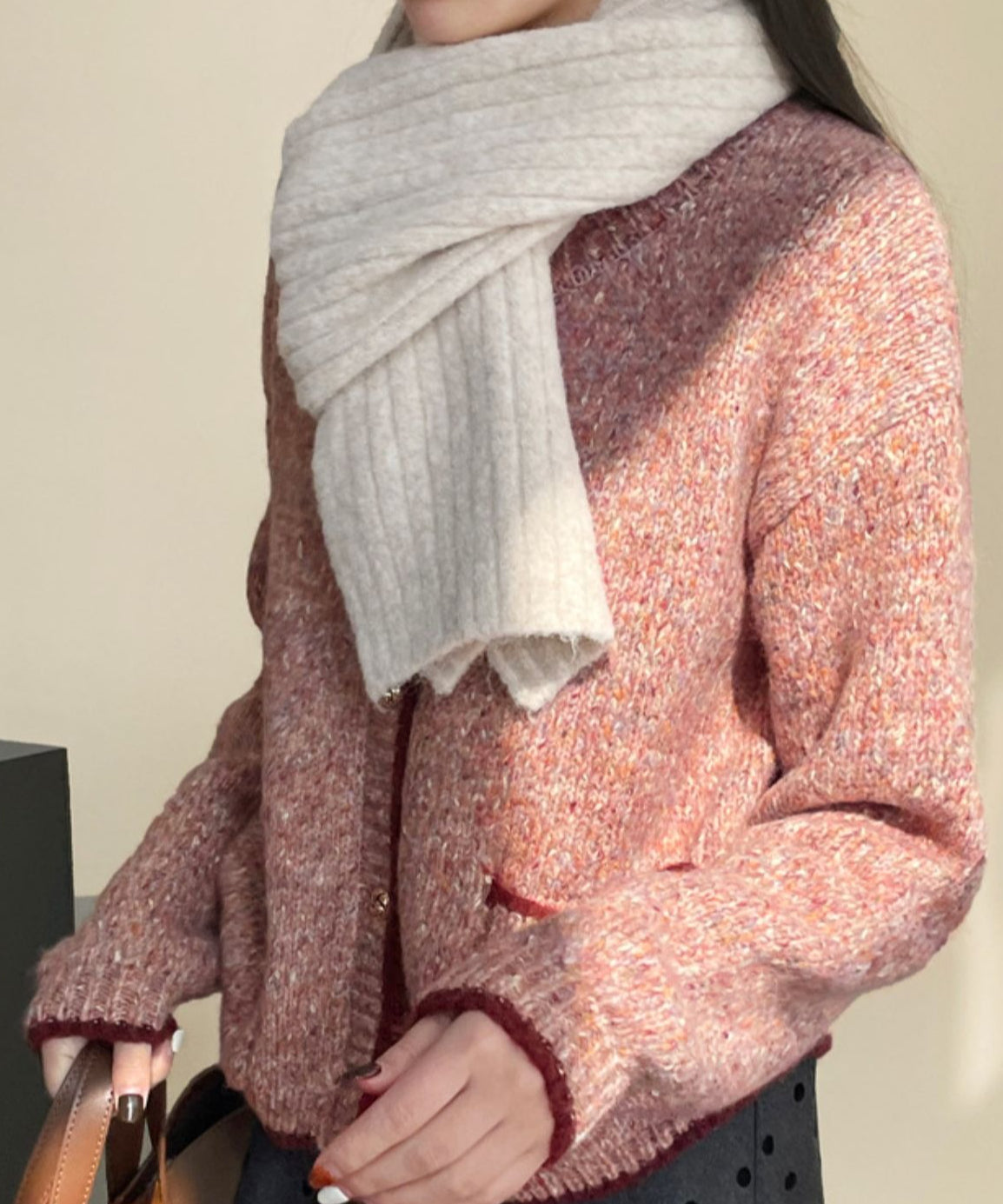ローズピンクのカーディガンを着用し、ベージュのマフラーを巻いた女性のバストアップ。ドット柄のボトムスと合わせた秋冬コーディネート。