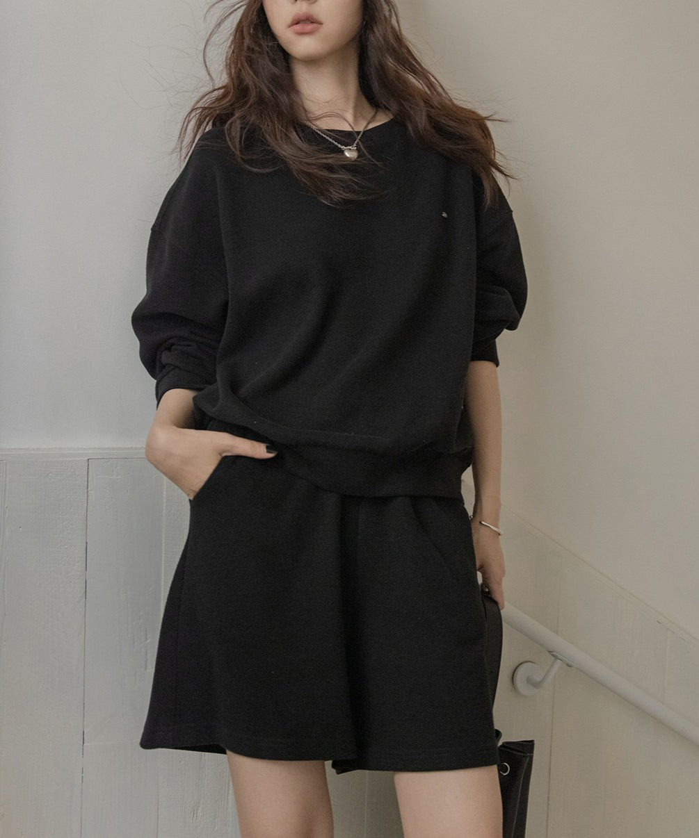 黒のセットアップを着用し、片手をポケットに入れた女性の全身。