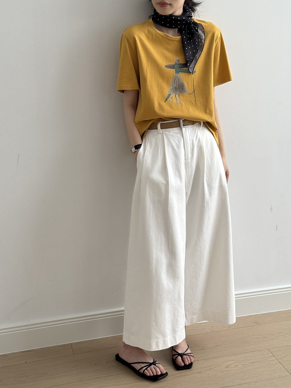 ホワイトのワイドパンツを履いたモデルが、黄色のプリントTシャツと黒いサンダルを合わせたコーディネート。