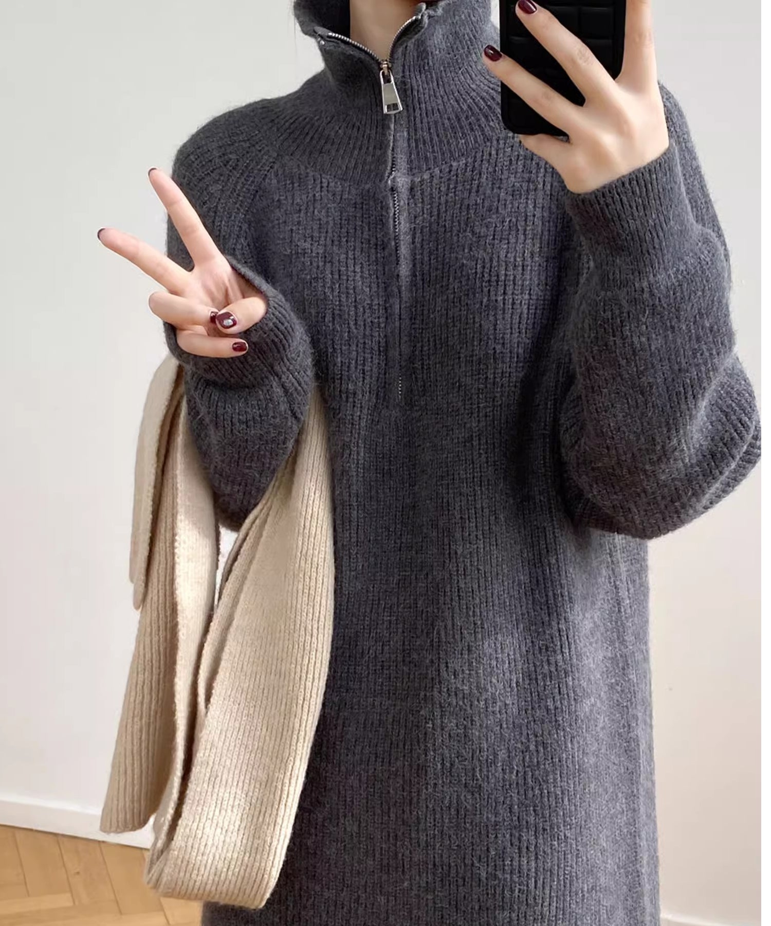 グレーのハーフジップニットロングワンピースを着用した女性が手にベージュのマフラーを持った写真。