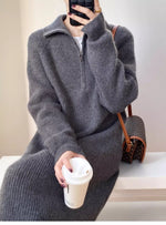 グレーのハーフジップニットロングワンピースを着用し、茶色のバッグと白いコーヒーカップを持つ女性のクローズアップ画像。