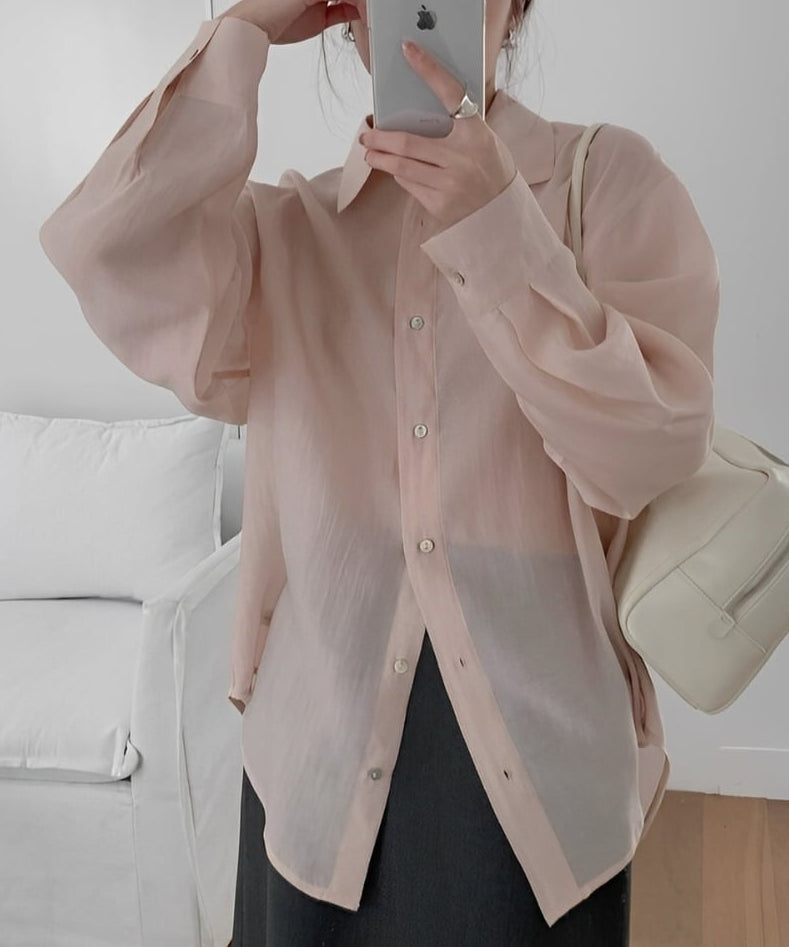 ピンクのシアー素材の長袖シャツを黒のロングスカートに合わせ、スマートフォンを構える女性のアップショット。