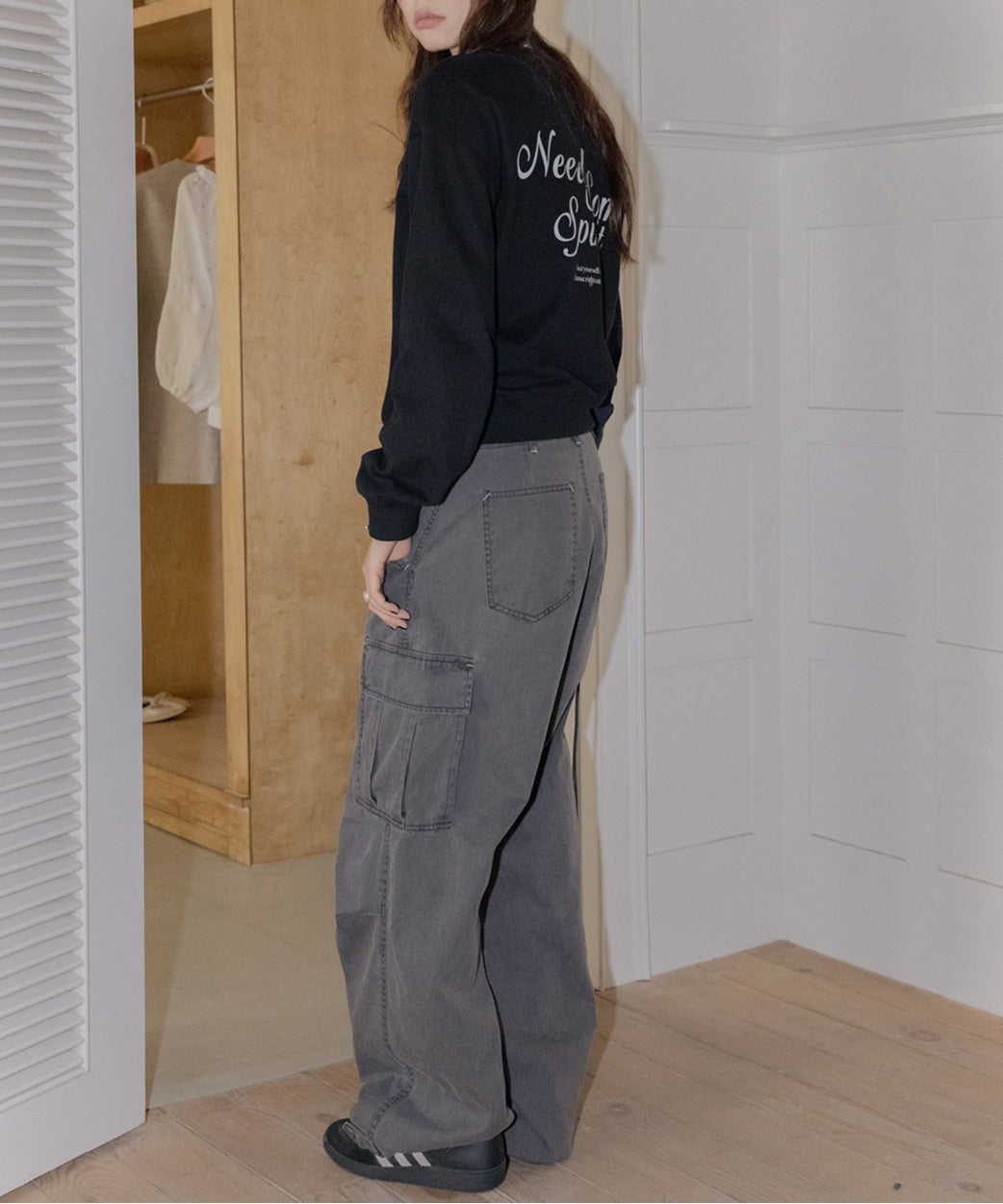 黒のスウェットを着用し、濃いグレーのデニムパンツを合わせた女性の横向きショット。背中に白いプリントロゴがある。