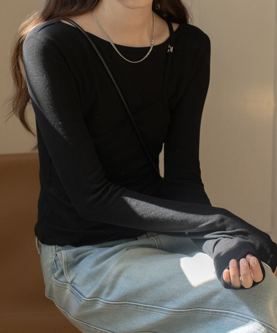 ブラックのレイヤードデザインのロングスリーブトップスを着用した女性の半身。トップスは胸元にキャミソールが重ねられたようなデザインで、黒のミニバッグを斜めがけし、シルバーのネックレスを着用した女性が座っている。