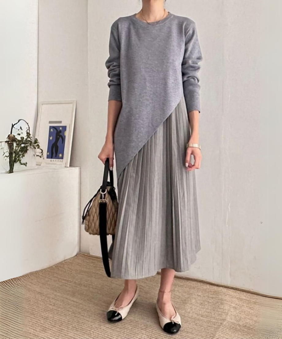 グレーのアシンメトリーニットとプリーツスカートのドレスを着用した女性
